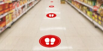 Floor graphics in red circles show recommended social distancing in a grocery store aisle.
