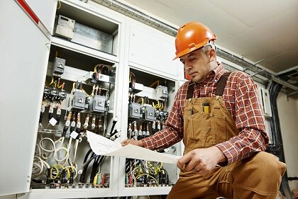 Electrician sitting in front of electric panel looking at blueprints
