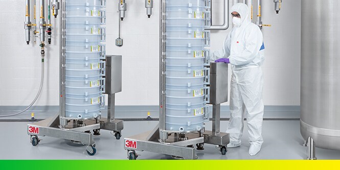 Engineer wearing mask and lab coat wheeling a 3M Encapsulated System Holder with 3M capsule products for bioprocessing
