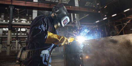 Welder wearing protective gear using a welding torch on a metal structure in a manufacturing plant
