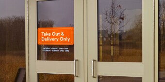 Image of a double door with a sign saying “Take Out & Delivery Only”
