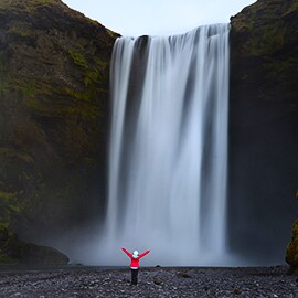 Image of person in a red coat standing in front of a large waterfall