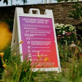 A close up shot of a Purple-red-colored sign outlining COVID-19 guidelines in a grassy area
