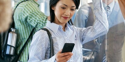 A smiling woman on a crowded subway looks at her smartphone.
