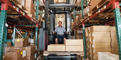Fork lift driver in a warehouse carrying a load of boxes.
