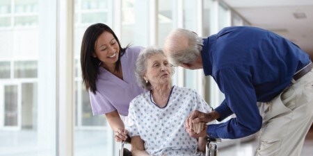 An elderly female in a wheelchair talking to an elderly male and a nurse
